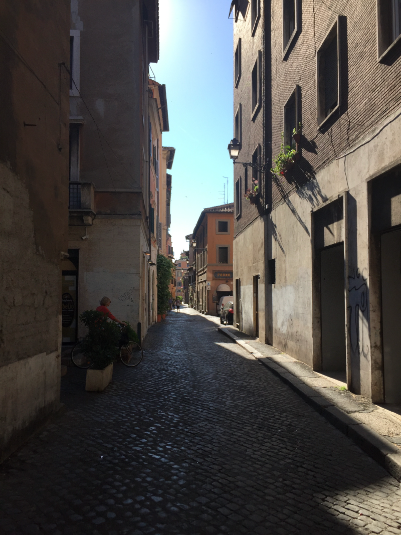 Narrow cobblestone street in Rome with old buildings and morning shadows