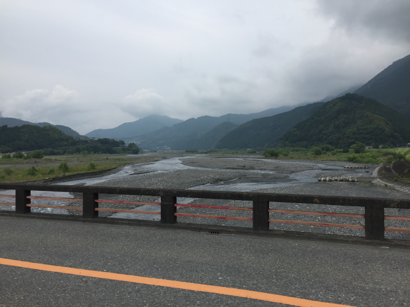 View from a bridge across a braided gravel riverbed toward cloud-shrouded mountains
