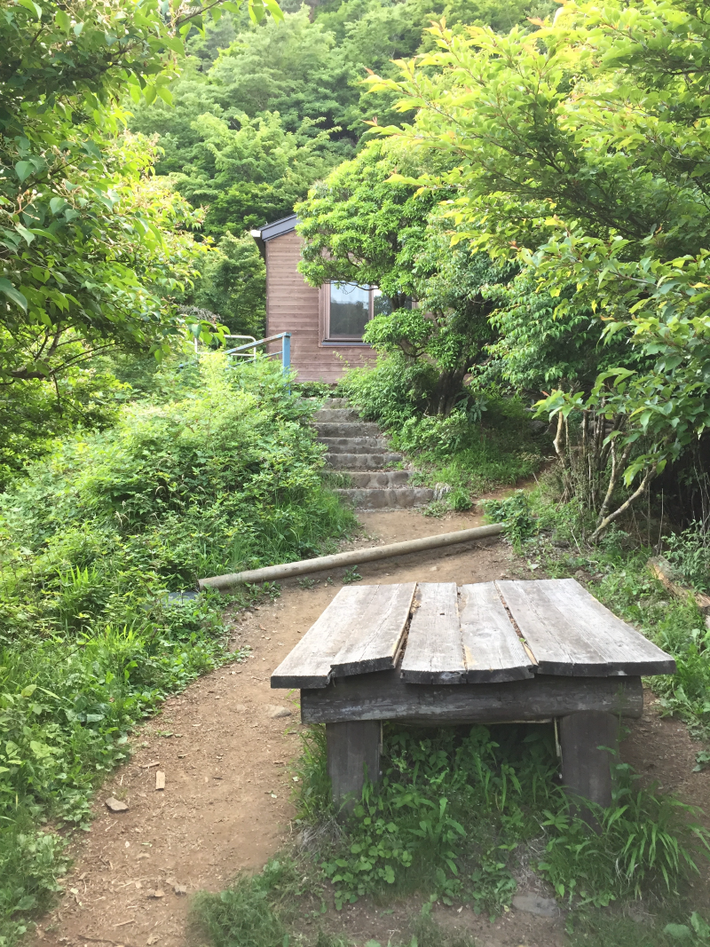 A small wooden hut perched above stone steps, a heavy plank table sitting on the path below