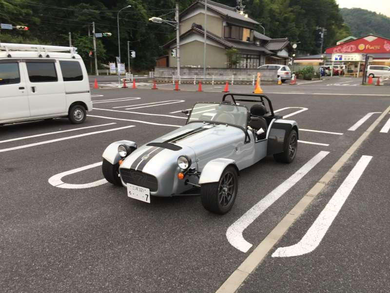Silver Caterham-style roadster parked in a lot with curved door-opening marks painted on the asphalt