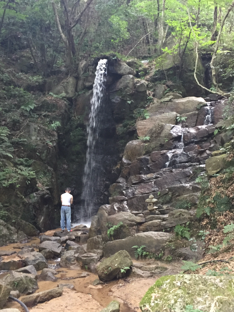 Person standing at base of tall waterfall cascading over rocks