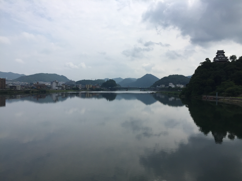 Calm river reflecting clouds with Inuyama Castle on forested hilltop
