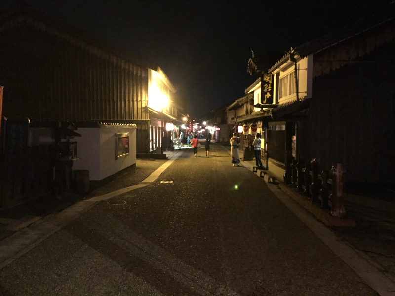 Quiet old-town street at night after the procession, a handful of figures in the distance under warm shop lights