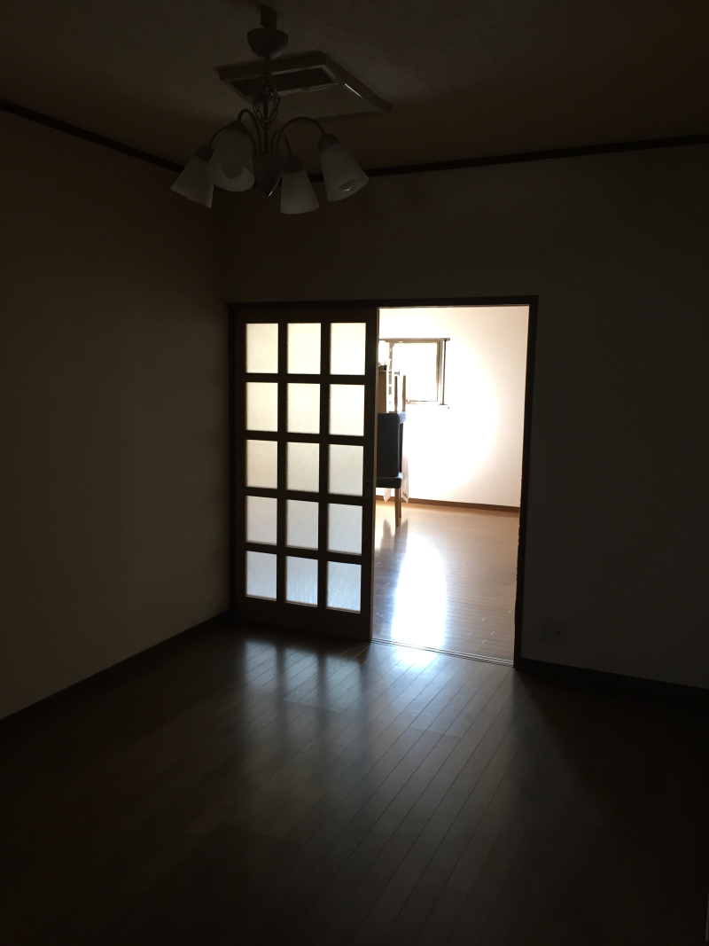Dim empty room with chandelier, sliding shoji door open to a brighter adjoining room