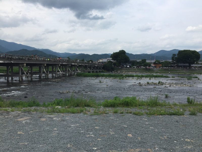 Long wooden Togetsukyo bridge crowded with people, crossing the shallow Katsura river under cloudy mountain sky