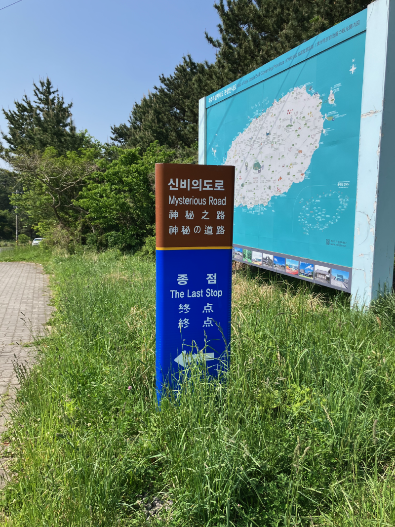 Blue Jeju Olle signpost beside road with island map
