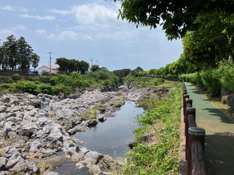 Rocky streambed beside wooden railing and paved riverside path
